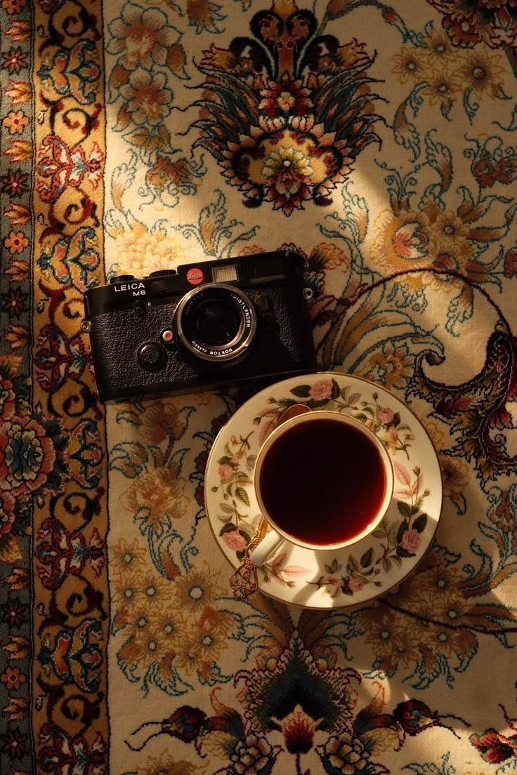 A camera and a cup of tea on a patterned carpet